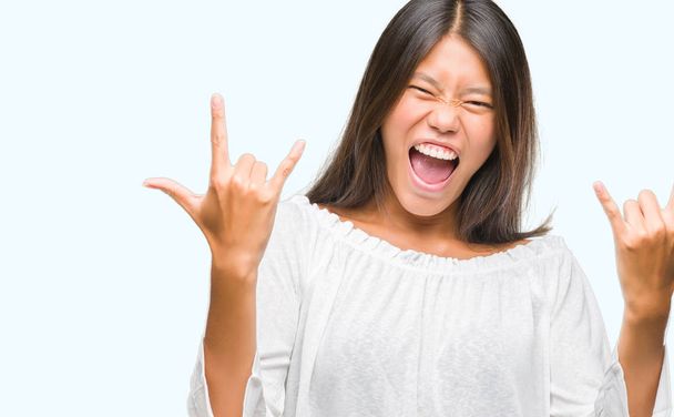 Молодая азиатка на изолированном фоне кричит с сумасшедшим выражением, делая рок-символ с поднятыми руками. Музыкант. Тяжёлая концепция
. - Фото, изображение