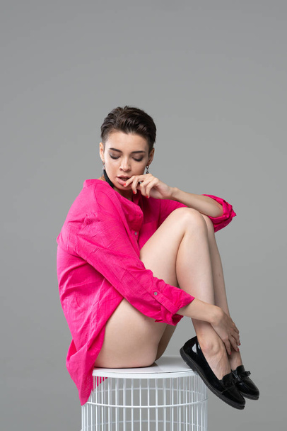 young beautiful girl posing nude in studio, sitting in red blouse - Photo, Image