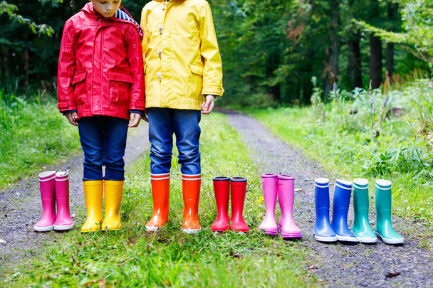 Pienet lapset, pojat ja tytöt värikkäissä sadesaappaissa. Lapset seisomassa syksyn metsässä. Koululaisten lähikuva ja erilaiset kumisaappaat. Jalkineet ja muoti sateinen lasku
 - Valokuva, kuva