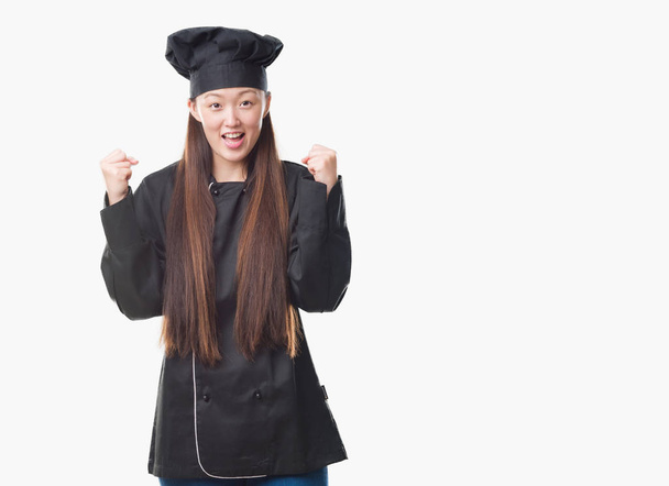 Joven mujer china sobre fondo aislado vistiendo uniforme de chef celebrando sorprendido y sorprendido por el éxito con los brazos levantados y los ojos abiertos. Concepto ganador
. - Foto, imagen
