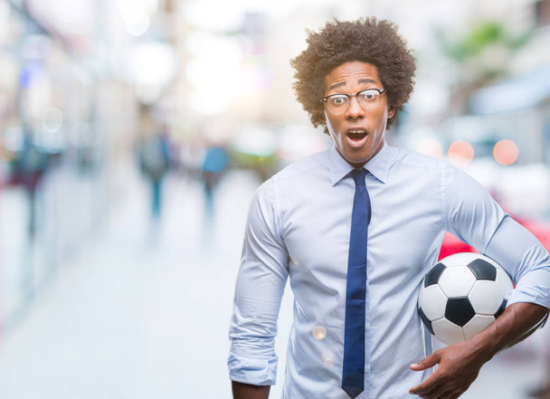 Afro-americano manager uomo tenendo palla da calcio su sfondo isolato spaventato in shock con una faccia a sorpresa, spaventato ed eccitato con espressione di paura
 - Foto, immagini