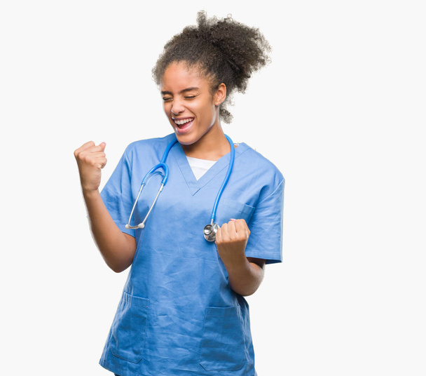 Młody lekarz z afro american kobieta na białym tle bardzo szczęśliwy i podekscytowany robi zwycięzca gest z podniesionymi rękami, uśmiechając się i krzyczy na sukces. Koncepcja celebracja. - Zdjęcie, obraz