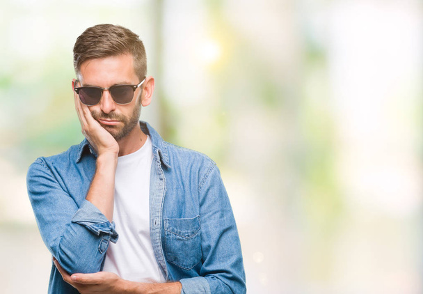 Young handsome man wearing sunglasses over isolated background thinking looking tired and bored with depression problems with crossed arms. - Photo, Image