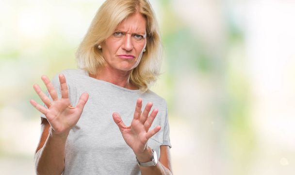 Middle age blonde woman over isolated background disgusted expression, displeased and fearful doing disgust face because aversion reaction. With hands raised. Annoying concept. - Foto, Imagem