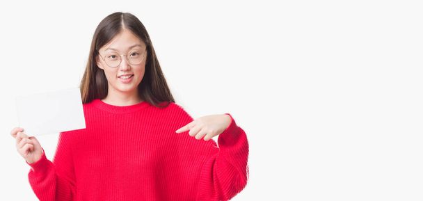 Jonge Chinese vrouw over geïsoleerde achtergrond met lege kaart met verrassing gezicht wijzende vinger naar zichzelf - Foto, afbeelding