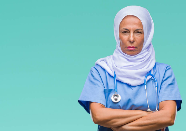 Mulher enfermeira árabe de meia idade usando hijab sobre fundo isolado cético e nervoso, desaprovando a expressão no rosto com os braços cruzados. Pessoa negativa
. - Foto, Imagem