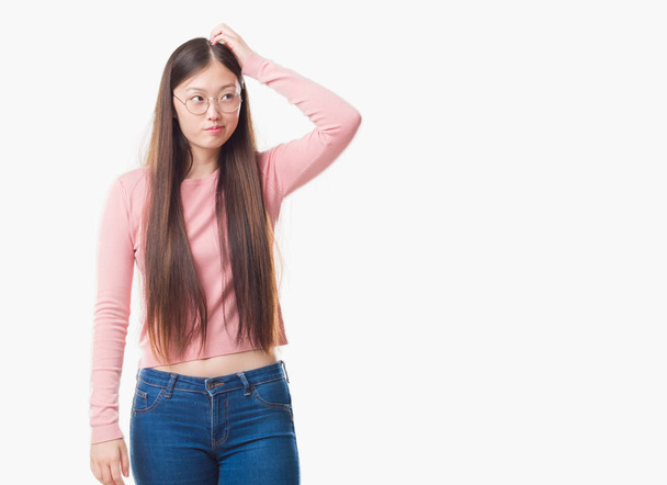 Giovane donna cinese su sfondo isolato indossando occhiali confondere e interrogare. Incerto con il dubbio, pensando con mano sulla testa. Concetto pensieroso
. - Foto, immagini