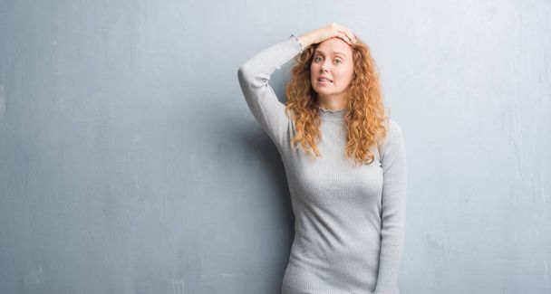 Young redhead woman over grey grunge wall stressed with hand on head, shocked with shame and surprise face, angry and frustrated. Fear and upset for mistake. - Foto, Bild