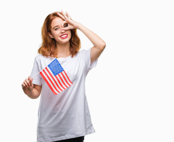 Giovane bella donna che tiene bandiera d'America su sfondo isolato con volto felice sorridente facendo ok segno con mano sugli occhi guardando attraverso le dita
 - Foto, immagini