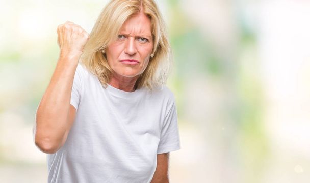 Blonde vrouw van middelbare leeftijd op geïsoleerde achtergrond boos en gekke verhogen vuist gefrustreerd en woedend terwijl schreeuwen met woede. Woede en agressief concept. - Foto, afbeelding
