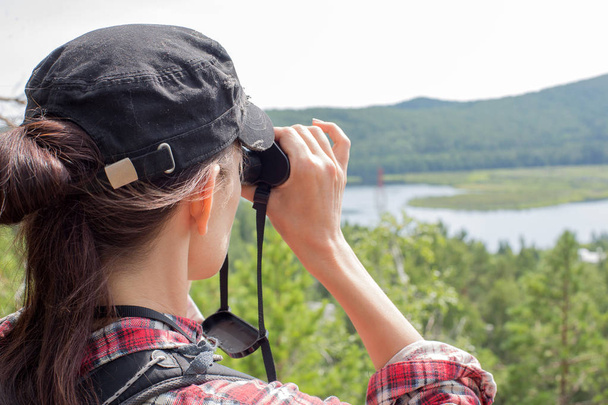 Турист с помощью бинокля смотрит на природу, озеро, гору и деревья крупным планом
 - Фото, изображение
