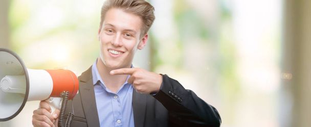 Jeune homme blond beau tenant un mégaphone très heureux pointant avec la main et le doigt
 - Photo, image