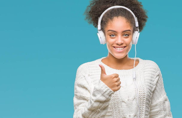 Young afro american woman wearing headphones over isolated background happy with big smile doing ok sign, thumb up with fingers, excellent sign - Foto, Bild