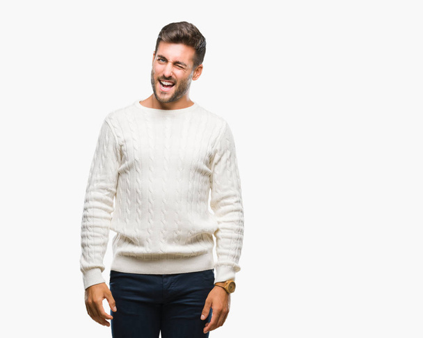 Jonge knappe man winter trui dragen over geïsoleerde achtergrond winking kijken naar de camera met sexy expressie, vrolijk en blij gezicht. - Foto, afbeelding
