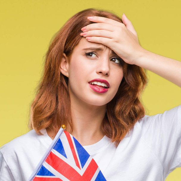Mladá krásná žena hospodářství vlajka Spojeného království izolované pozadí zdůraznil, s rukou na hlavě, šokován studem a překvapením čelí, naštvaný a frustrovaný. Strachu a rozrušení pro chybu. - Fotografie, Obrázek