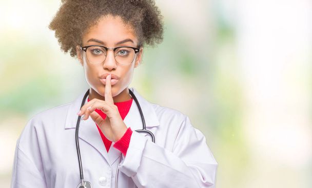 Genç afro Amerikalı doktor kadın dudaklarında parmak ile sessiz olmanı izole arka plan yüzünden. Sessizlik ve gizli kavramı. - Fotoğraf, Görsel
