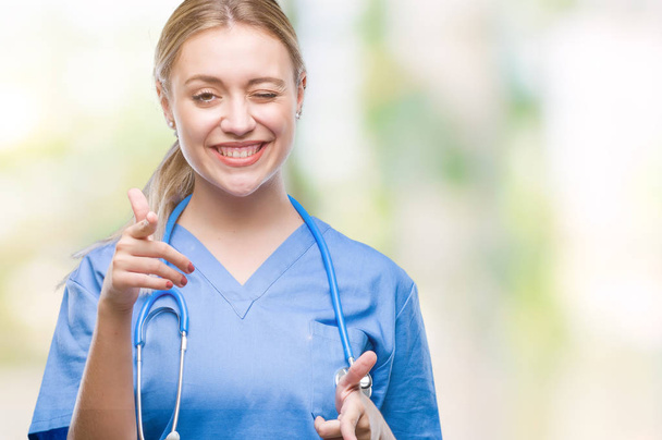 Young blonde surgeon doctor woman over isolated background pointing fingers to camera with happy and funny face. Good energy and vibes. - 写真・画像