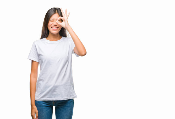 Young asian woman over isolated background doing ok gesture with hand smiling, eye looking through fingers with happy face. - Foto, afbeelding