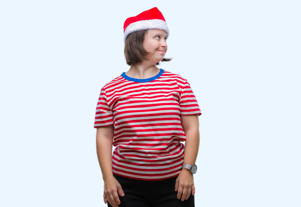 Fiatal felnőtt nő visel karácsonyi kalap alatt down-szindrómás elszigetelt háttér keres el az oldalon mosollyal arcán, természetes kifejezése. Nevetve magabiztos. - Fotó, kép
