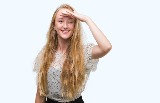 Blond dospívající žena nosí tričko Krtek velmi šťastný a usmívající se, hledá daleko s rukou přes hlavu. Hledání koncepcí. - Fotografie, Obrázek