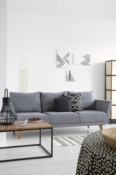 Lanterna sul tavolo vicino divano grigio in bianco soggiorno interno con manifesti sulla parete. Foto reale
 - Foto, immagini