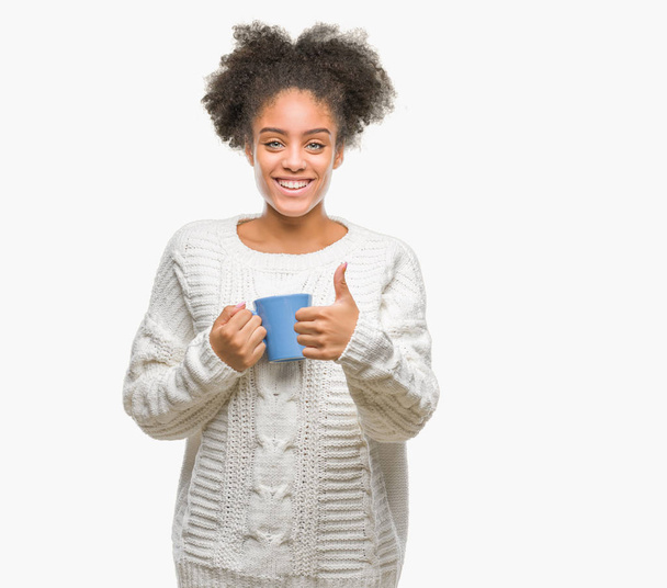 Młodych afro american kobieta driking filiżankę kawy na białym tle szczęśliwy z duży uśmiech robi znak ok, kciuk palcami, bardzo dobry znak - Zdjęcie, obraz