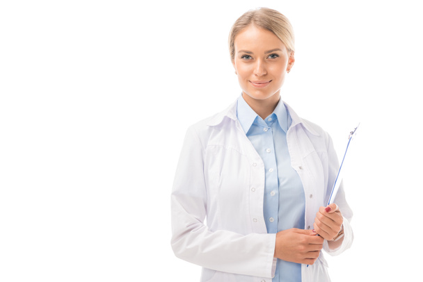 smiling young female doctor with clipboard looking at camera isolated on white - Фото, изображение