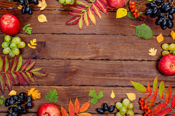 Autumn leaves with apples and grapes on wooden background - Foto, afbeelding