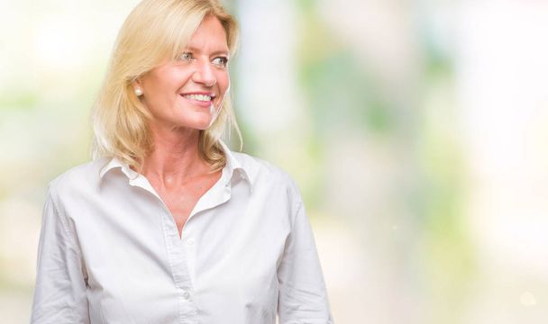 Middle age blonde business woman over isolated background looking away to side with smile on face, natural expression. Laughing confident. - Photo, Image
