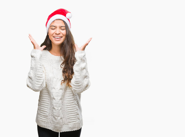 Nuori arabinainen yllään joulu hattu yli eristetty tausta juhlii hullu ja hullu menestystä kädet kohotetaan ja suljetut silmät huutaa innoissaan. Voittajan käsite
 - Valokuva, kuva