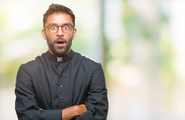 Volwassen hispanic katholieke priester man over geïsoleerde achtergrond bang en geschokt met verrassing meningsuiting, angst en opgewonden gezicht. - Foto, afbeelding