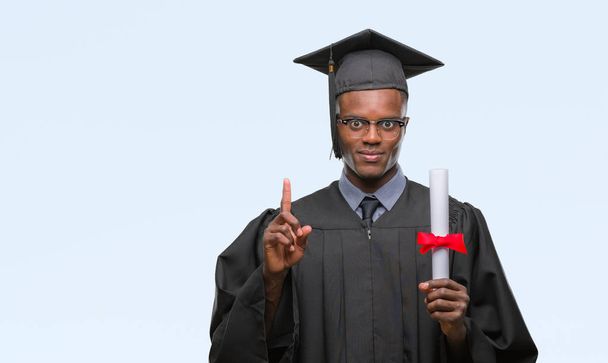 Young graduated african american man holding degree over isolated background surprised with an idea or question pointing finger with happy face, number one - Photo, image