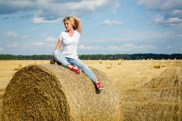 Felice giovane donna seduta su rotolo di paglia in campo
 - Foto, immagini