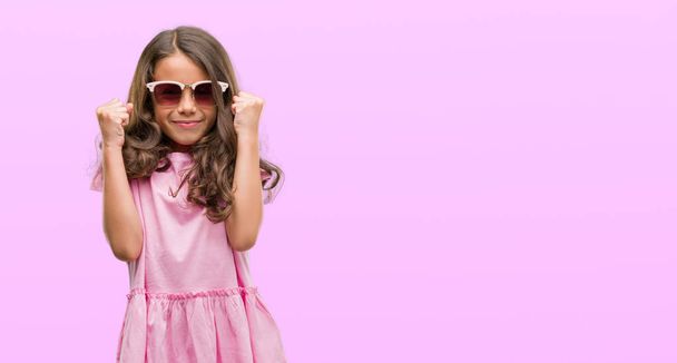 Brunetka hispánský dívka nosí sluneční brýle křičí hrdá a slaví vítězství a úspěch, velmi vzrušený, fandění emoce - Fotografie, Obrázek