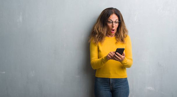 Spaanse vrouw middenleeftijd smartphone bang in schok met een verrassing gezicht, bang en opgewonden met angst expressie - Foto, afbeelding