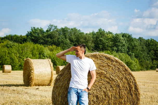 Щасливий усміхнений чоловік стоїть біля стопки сіна в пшеничному полі
 - Фото, зображення