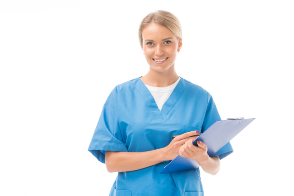 smiling young nurse writing in clipboard and looking at camera isolated on white - Photo, image