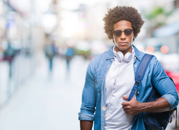 afro-americano homem vestindo fones de ouvido e mochila sobre fundo isolado com uma expressão confiante no rosto inteligente pensando sério
 - Foto, Imagem