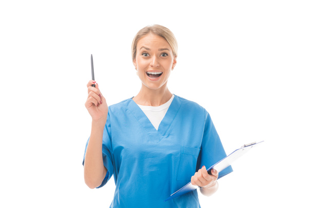 expressive young nurse with creative idea holding clipboard and pointing up isolated on white - Foto, immagini
