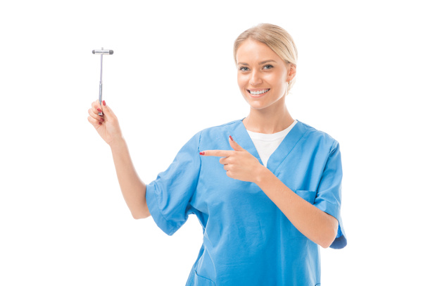 smiling young neurologist pointing at reflex hammer isolated on white - Photo, Image