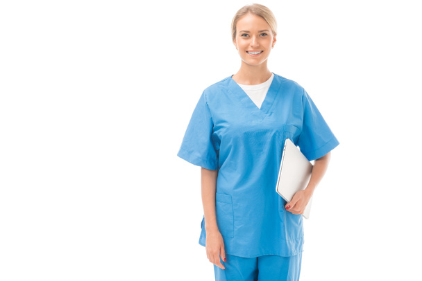 enfermera joven sonriente con portátil mirando a la cámara aislada en blanco
 - Foto, Imagen