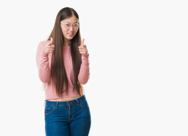 Jonge Chinese vrouw over geïsoleerde achtergrond bril wijzen vingers naar camera met gelukkig en grappig gezicht. Goede energie en vibrafoon. - Foto, afbeelding