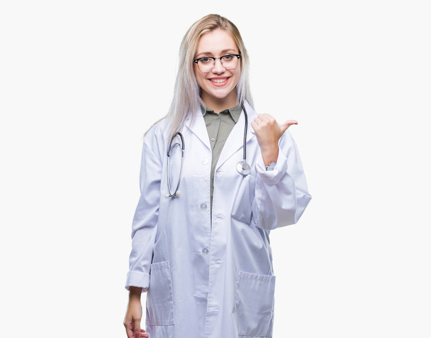 Молода блондинка лікарка над ізольованим тлом посміхається з щасливим обличчям, дивлячись і вказуючи на бік з великим пальцем вгору
. - Фото, зображення