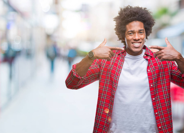Hombre afroamericano sobre fondo aislado sonriendo confiado mostrando y señalando con los dedos los dientes y la boca. Concepto de salud
. - Foto, imagen