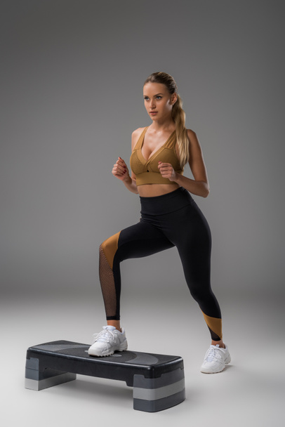 mujer joven y deportiva haciendo ejercicio en el tablero de aeróbicos paso en gris
 - Foto, Imagen