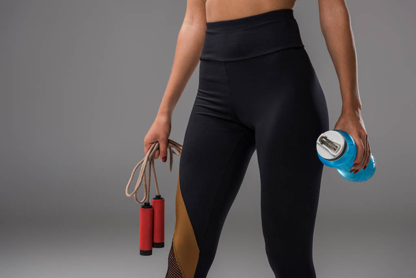 cropped shot of sportive woman in leggins with jumping rope and water bottle on grey - Photo, Image
