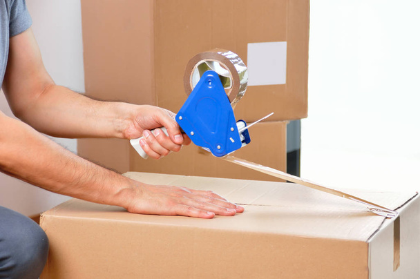 Shot of an unidentifiable young man closing a cardboard box with tape at home - 写真・画像