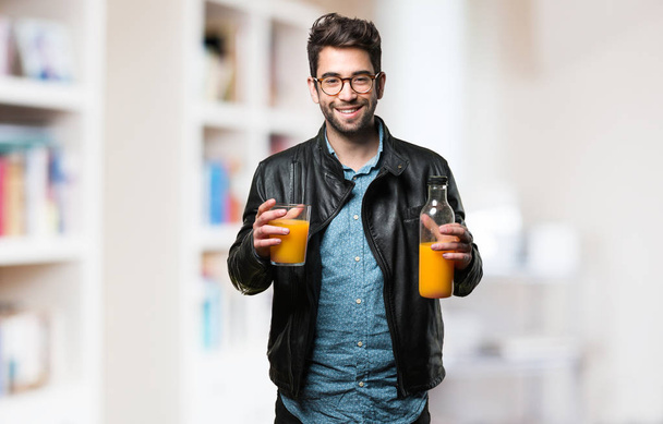 young man holding an orange juice bottle on blurred background - Фото, изображение