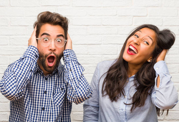 Young indian woman and caucasian man couple surprised and shocked, looking with wide eyes, excited by an offer or by a new job, win concept - Photo, Image