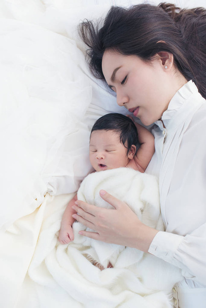 Happy beautiful asian woman black hair in white suit looking at her sleeping baby child in arm - Φωτογραφία, εικόνα